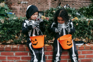 Little multiracial girls in skeleton costumes sitting with candy bucket
