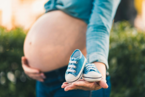 A pregnant woman holding shoe for her upcoming cute baby