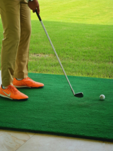 a golf player is standing on grassroots putting mat with his golf stick and ball