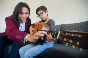 A Man Teaching a Boy to Play the Guitar
