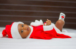 Baby Wearing Santa Claus Costume While Lying on Bed
