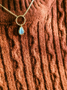 A Necklace with Light Blue Pendant on Brown Sweater