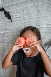 Girl with artificial teeth with pumpkins on eyes wearing black T-shirt
