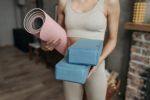 A woman is holding two yoga block and a yoga mat in her hands