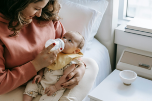 Smiling young mother feeding baby with milk from bottle