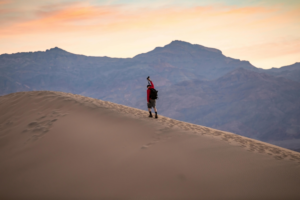 A Man Walking on a Large Dune at Sunset