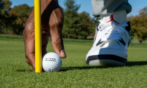 a man is practicing golf  wearing white color shoes