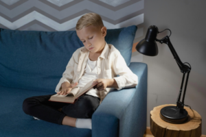 A Boy Reading a Book while Sitting on a Blue Couch