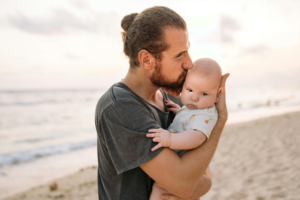 Man in Black Crew Neck T-shirt Carrying Baby on the Beach