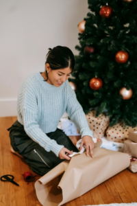 Smiling Asian woman wrapping present near Christmas tree
