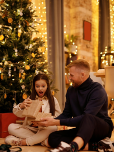 Surprised girl opening gift box near smiling father in house
