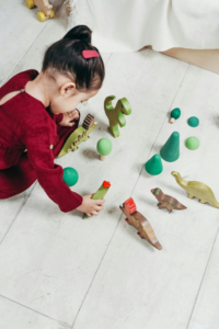 Girl in Red Long Sleeve Dress Sitting on White Floor Tiles Playing with Toys
