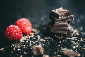 Stacked Chocolates Bars Beside Raspberries
