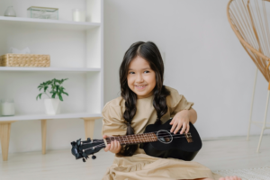 A Girl Playing a Ukulele while Smiling
