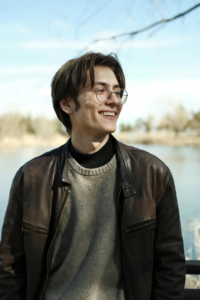 A Man In a Brown Leather Jacket on a Gray Sweater Standing by the River